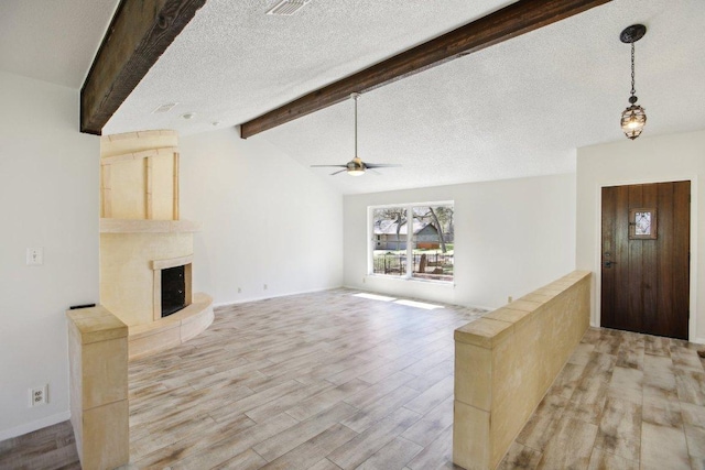 unfurnished living room with a large fireplace, light wood finished floors, lofted ceiling with beams, ceiling fan, and a textured ceiling