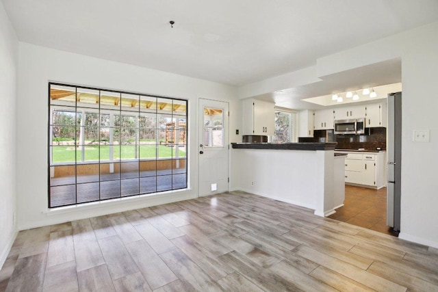 kitchen featuring white cabinets, a peninsula, stainless steel appliances, and backsplash