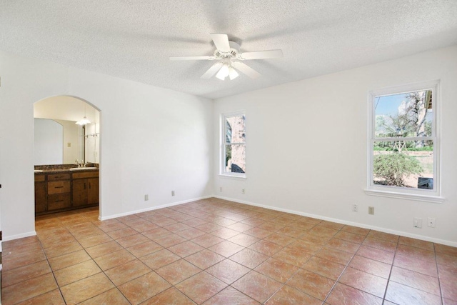 spare room with light tile patterned floors, ceiling fan, arched walkways, and a sink