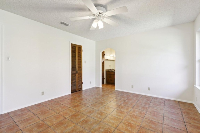 unfurnished room with arched walkways, light tile patterned floors, visible vents, a ceiling fan, and a textured ceiling