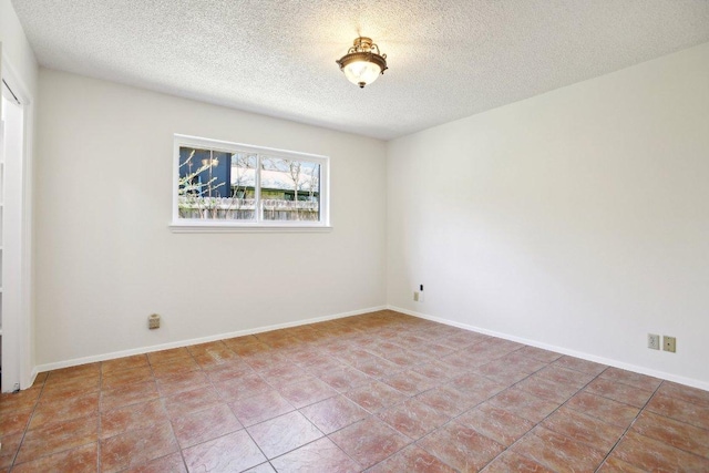 tiled empty room with a textured ceiling and baseboards