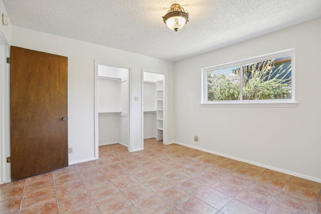 unfurnished bedroom with a textured ceiling, multiple closets, and baseboards