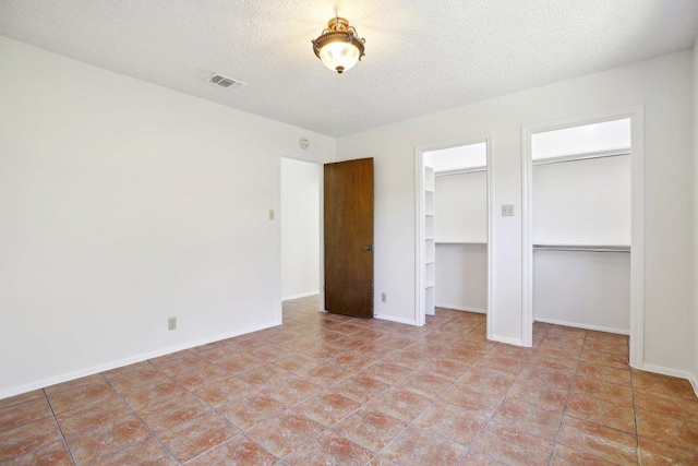 unfurnished bedroom featuring baseboards, a textured ceiling, visible vents, and two closets