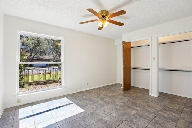 unfurnished bedroom with baseboards, multiple windows, a textured ceiling, and multiple closets