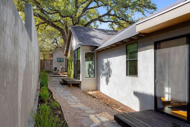 view of side of property featuring fence, metal roof, and stucco siding