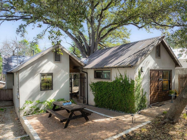 rear view of property featuring fence, metal roof, and stucco siding