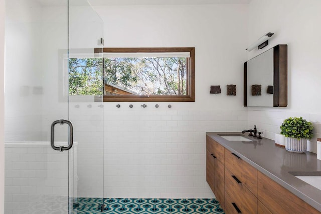 full bathroom with double vanity, a stall shower, tile walls, and a sink