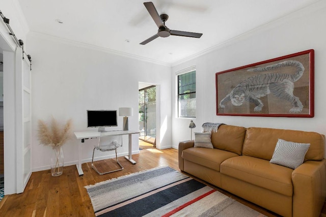 living room with ceiling fan, a barn door, hardwood / wood-style floors, and crown molding