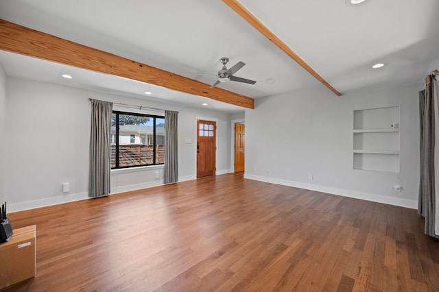 unfurnished living room with beamed ceiling, built in features, baseboards, and wood finished floors