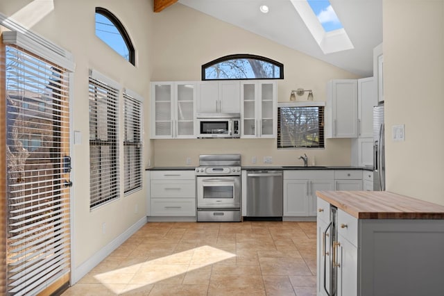 kitchen with glass insert cabinets, appliances with stainless steel finishes, a skylight, wood counters, and a sink