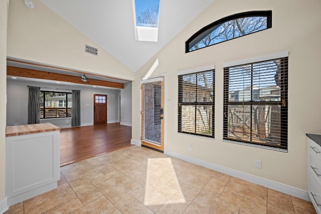 entrance foyer featuring a skylight, light tile patterned floors, visible vents, and high vaulted ceiling