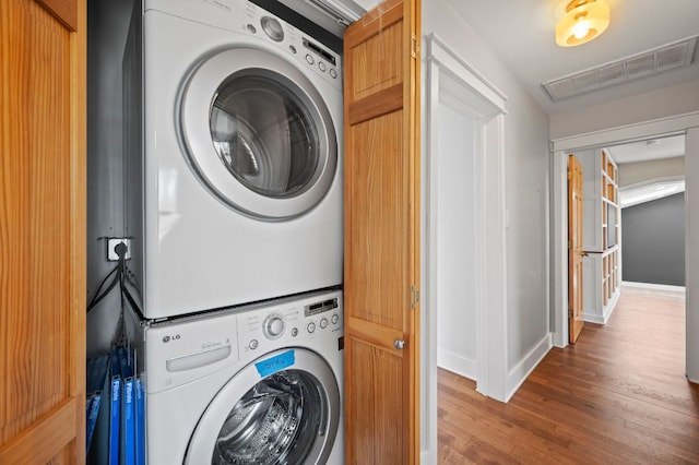 laundry room with visible vents, baseboards, stacked washer and dryer, laundry area, and wood finished floors