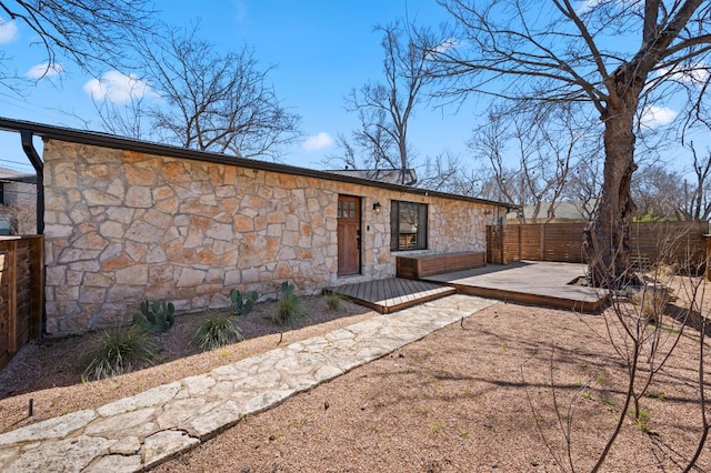 exterior space with a wooden deck, stone siding, and fence