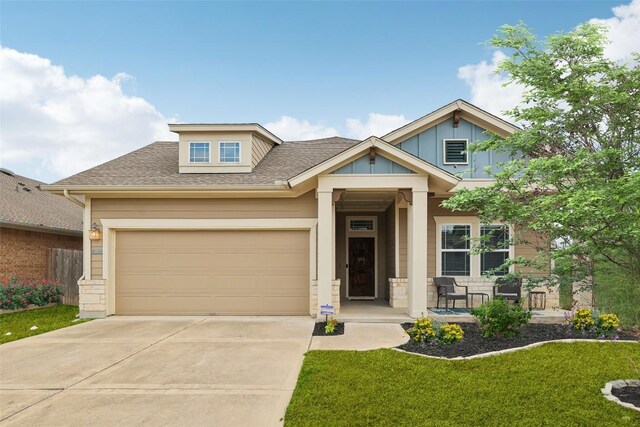 craftsman-style home with a shingled roof, concrete driveway, covered porch, board and batten siding, and a front yard