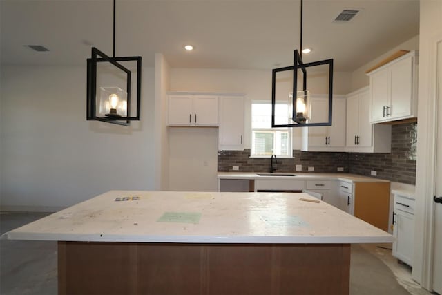 kitchen featuring tasteful backsplash, visible vents, a center island, white cabinetry, and a sink