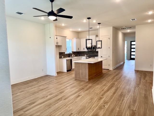 kitchen with decorative backsplash, appliances with stainless steel finishes, baseboards, open floor plan, and light wood-style floors