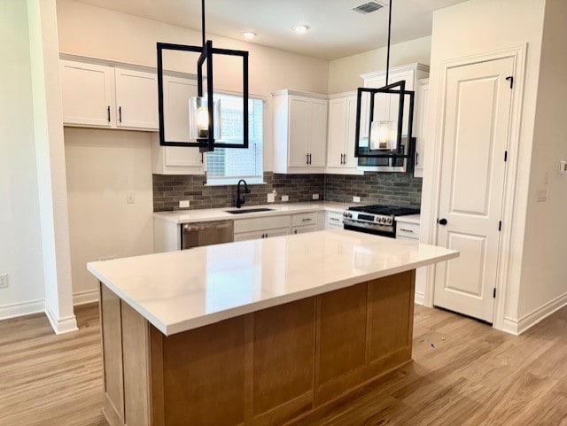 kitchen with white cabinets, a sink, light wood-style floors, stainless steel appliances, and backsplash