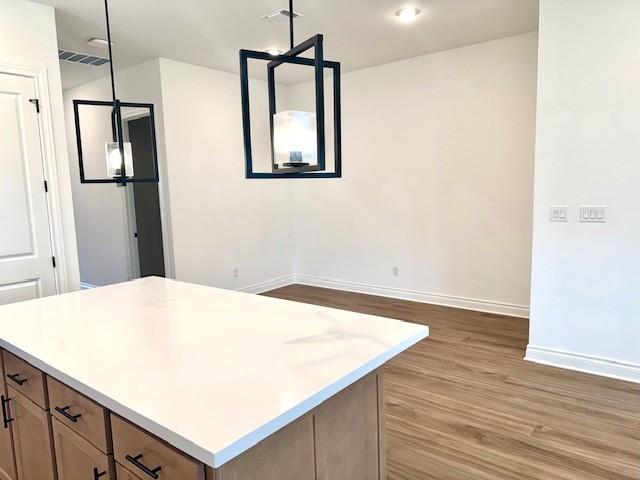 kitchen featuring visible vents, wood finished floors, baseboards, a center island, and light countertops