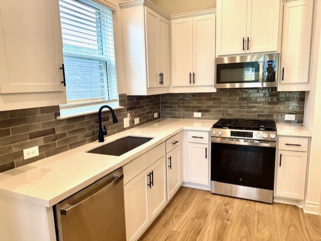 kitchen with decorative backsplash, appliances with stainless steel finishes, a sink, white cabinets, and light wood-style flooring