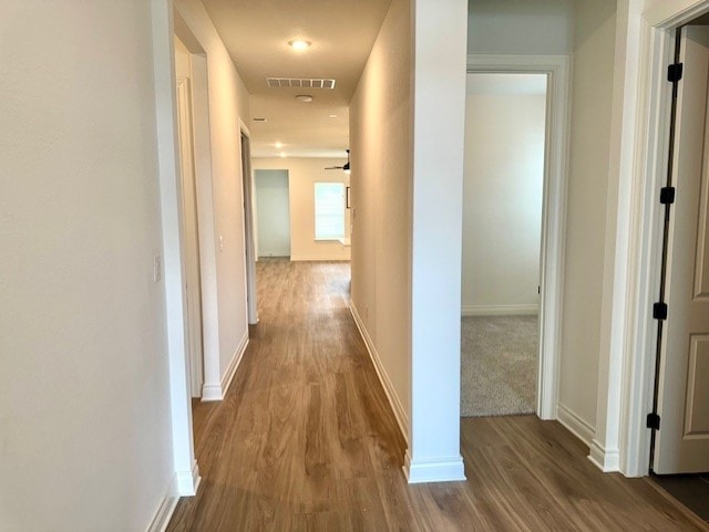 hall with baseboards, wood finished floors, and visible vents