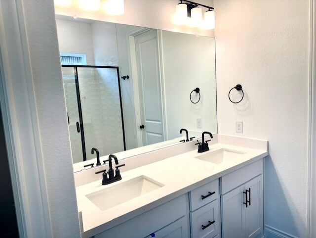 full bath with a sink, a textured wall, a shower stall, and double vanity