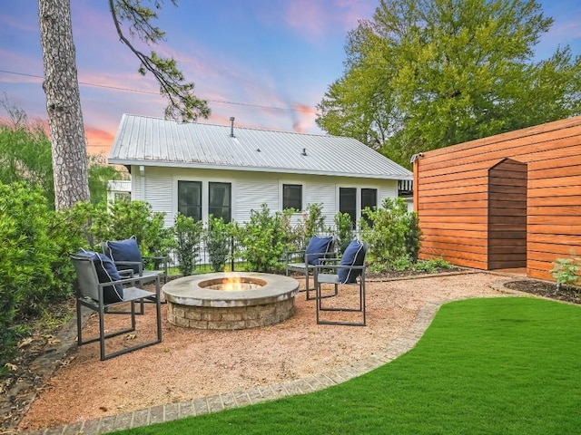 back of house at dusk with a yard, metal roof, an outdoor fire pit, and a patio area