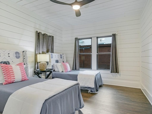 bedroom featuring wooden walls, dark wood-type flooring, a ceiling fan, and baseboards