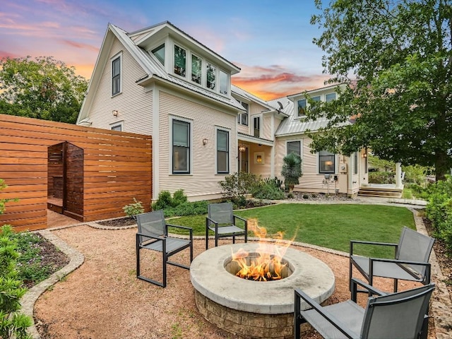 rear view of house featuring fence, a fire pit, metal roof, and a yard