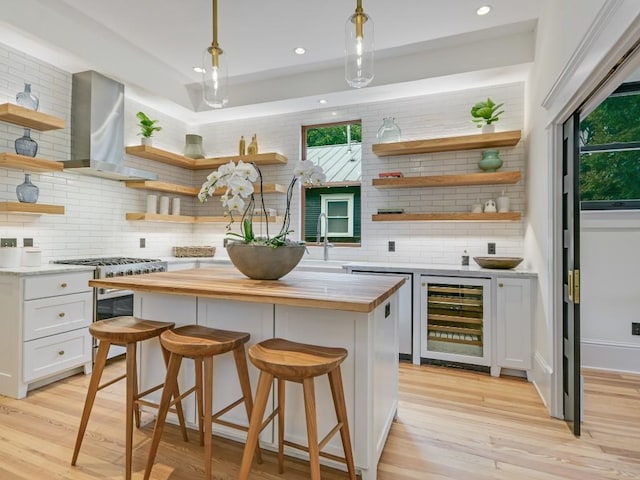 kitchen featuring open shelves, wine cooler, wall chimney exhaust hood, and butcher block countertops