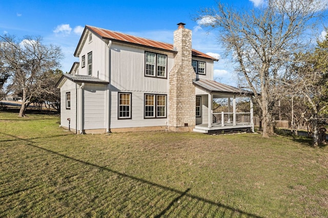 rear view of property with a standing seam roof, metal roof, a chimney, and a lawn