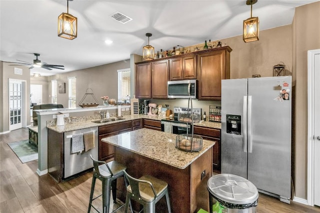 kitchen featuring stainless steel appliances, visible vents, a sink, wood finished floors, and a peninsula