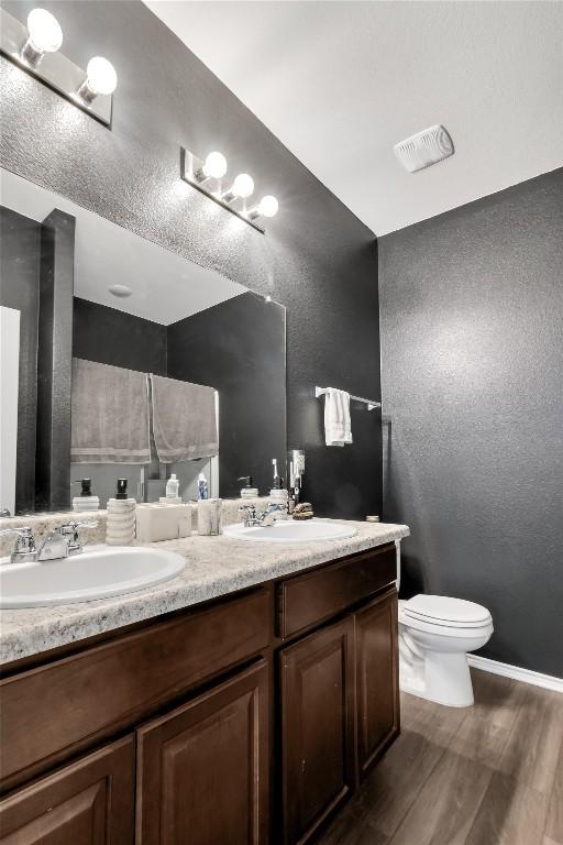 bathroom with visible vents, a sink, toilet, and double vanity