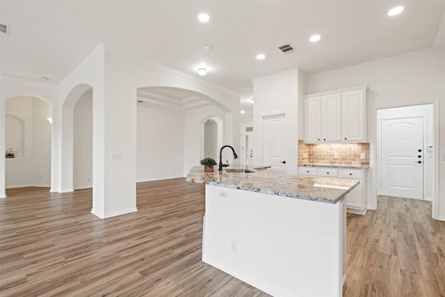 kitchen featuring tasteful backsplash, visible vents, light stone countertops, white cabinetry, and a sink