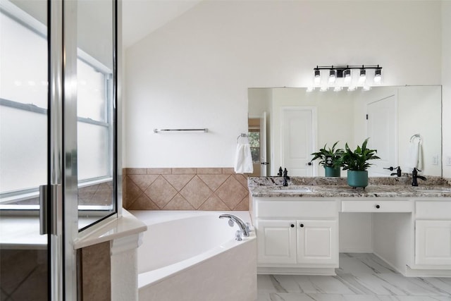 full bath with a garden tub, a sink, vaulted ceiling, marble finish floor, and double vanity