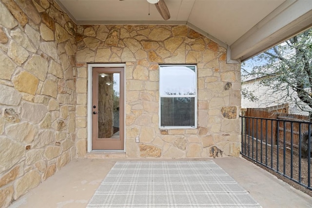 doorway to property with ceiling fan, stone siding, and fence