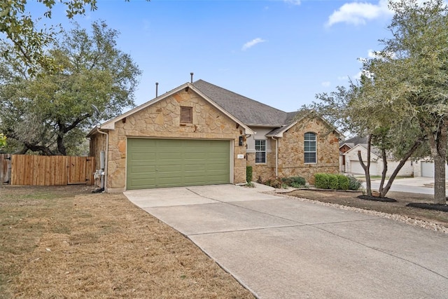 view of front of property with concrete driveway, stone siding, an attached garage, a gate, and fence