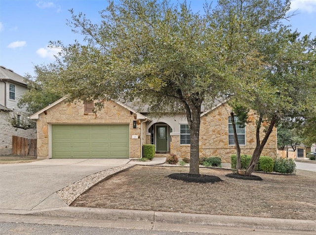 view of front of house with an attached garage, stone siding, fence, and concrete driveway