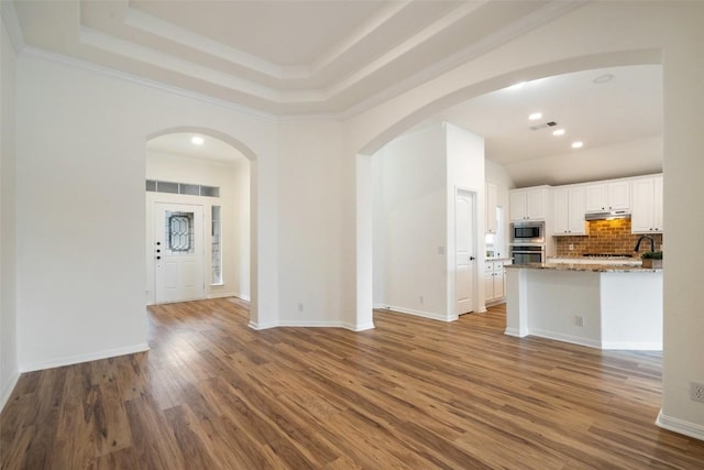 interior space featuring baseboards, visible vents, arched walkways, wood finished floors, and a tray ceiling