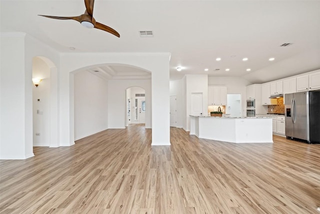 unfurnished living room featuring light wood finished floors, visible vents, arched walkways, and crown molding