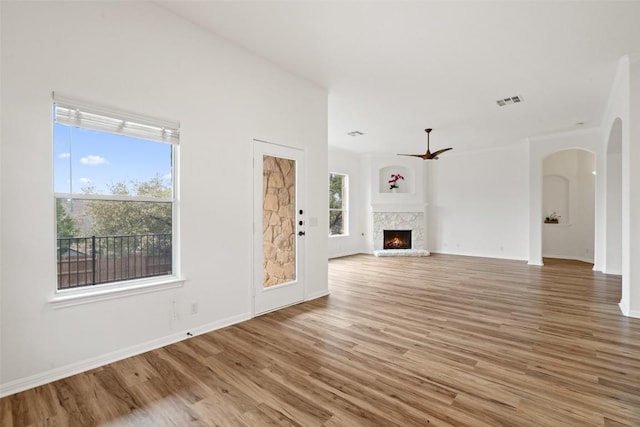 unfurnished living room featuring visible vents, arched walkways, baseboards, a lit fireplace, and light wood-type flooring