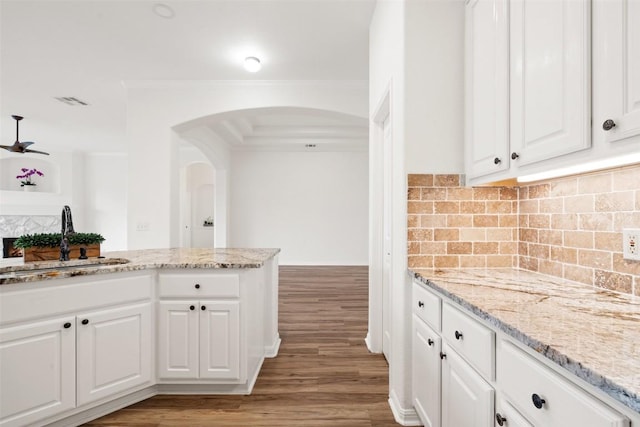 kitchen featuring light wood-style flooring, arched walkways, backsplash, and a sink