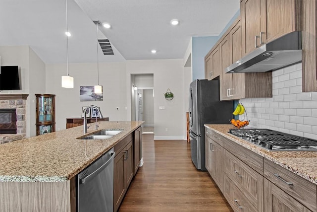 kitchen featuring light stone counters, under cabinet range hood, dark wood-style flooring, a sink, and appliances with stainless steel finishes