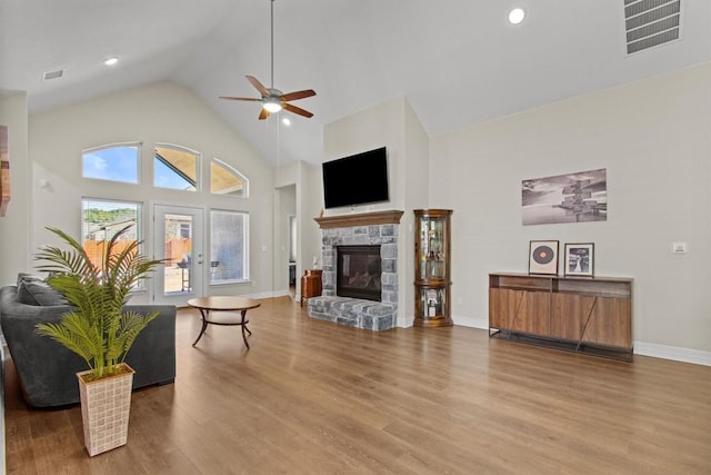 living room featuring high vaulted ceiling, a fireplace, visible vents, and wood finished floors