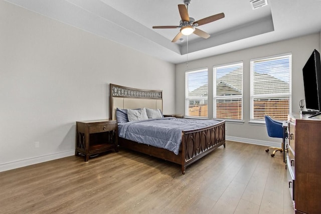 bedroom with a tray ceiling, light wood-type flooring, visible vents, and baseboards