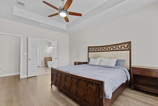 bedroom with baseboards, visible vents, a tray ceiling, and wood finished floors