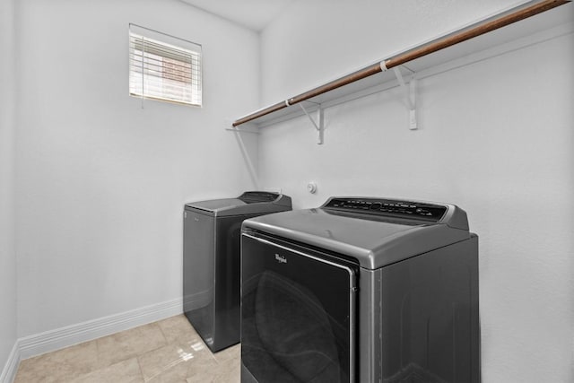 clothes washing area featuring laundry area, light tile patterned flooring, washing machine and clothes dryer, and baseboards