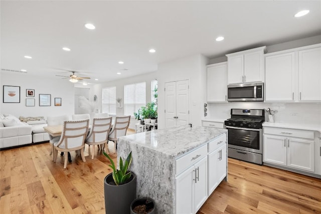 kitchen with ceiling fan, white cabinetry, open floor plan, stainless steel appliances, and light wood-style flooring