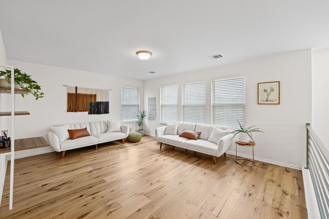 living room with light wood-type flooring, visible vents, plenty of natural light, and baseboards