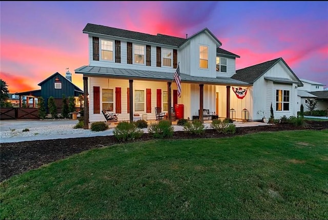 back of property featuring a standing seam roof, metal roof, covered porch, a lawn, and board and batten siding