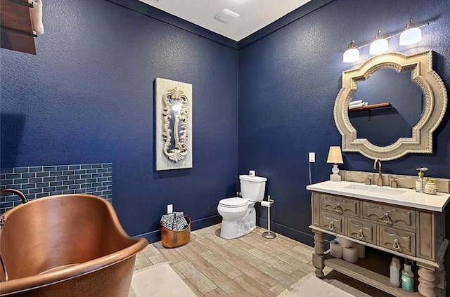 bathroom with a textured wall, toilet, a soaking tub, wood finished floors, and vanity